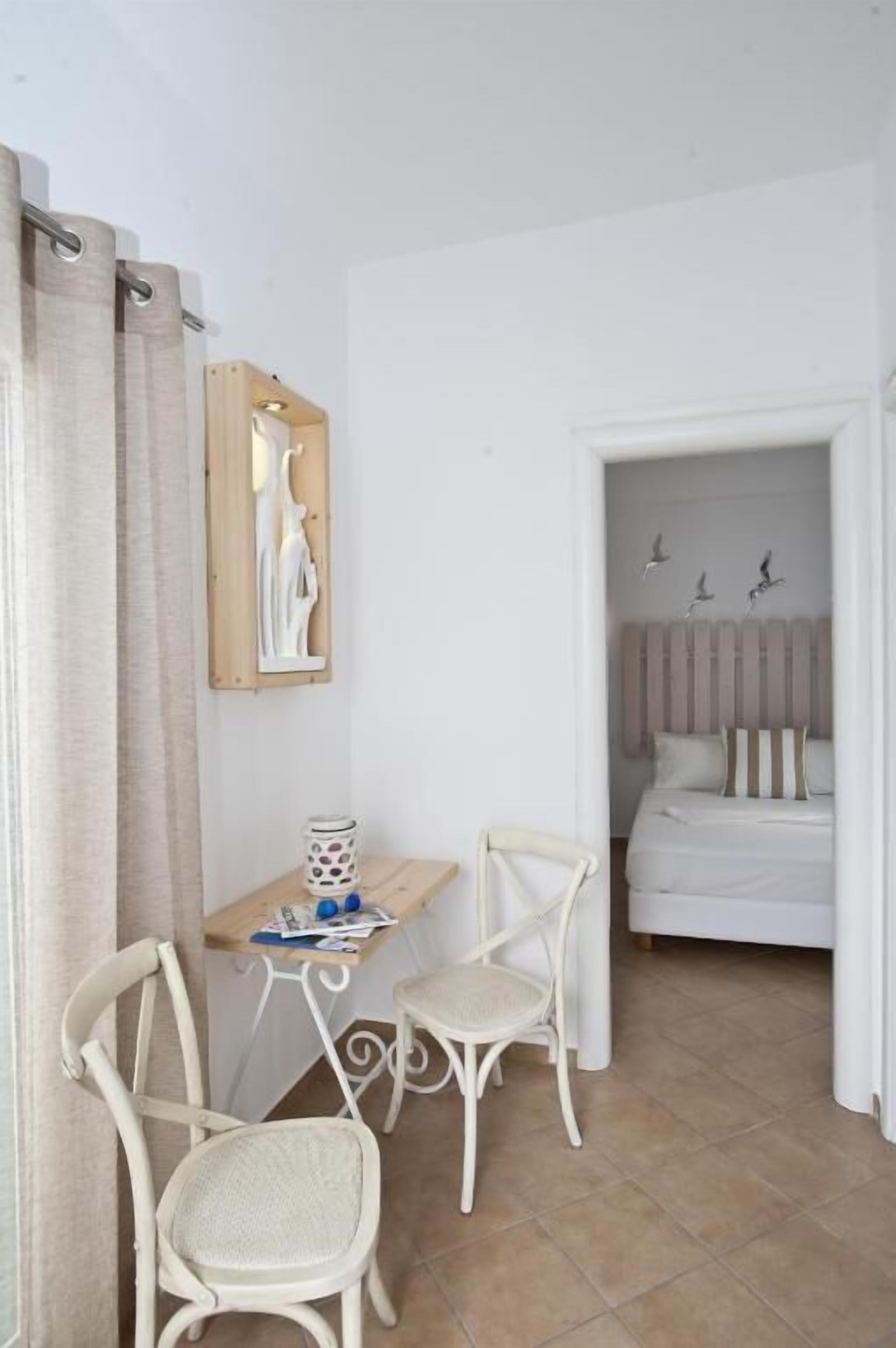 A room with a bed, a desk, two chairs, a wall-mounted artwork, and a ceiling light fixture.