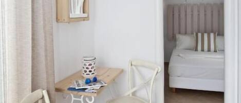 A room with a bed, a desk, two chairs, a wall-mounted artwork, and a ceiling light fixture.