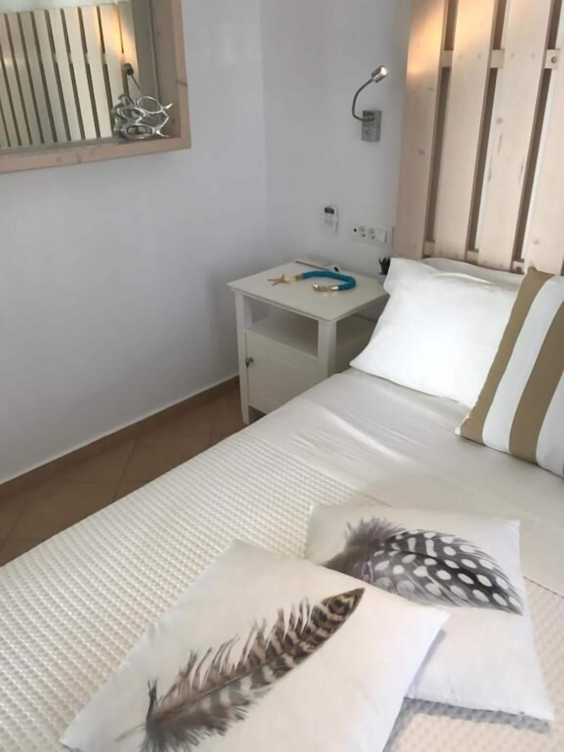 Un dormitorio ordenado con cama, almohadas, una mesita de noche y un pequeño escritorio.