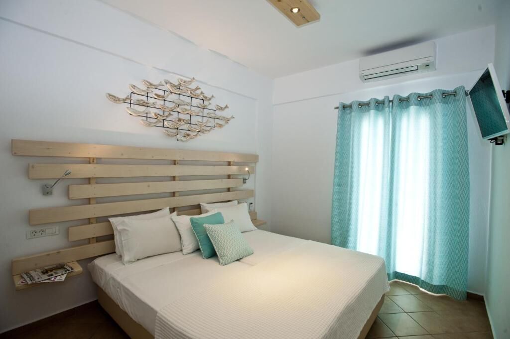 A bedroom with a wooden headboard, a bed with white bedding and a teal pillow, a wall-mounted air conditioner, and a window with teal curtains.