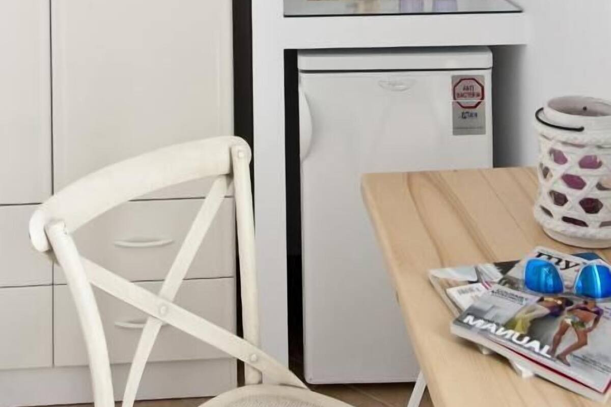 A small kitchenette with a refrigerator, a microwave, and a coffee maker. There is a white cabinet and a chair in the room.