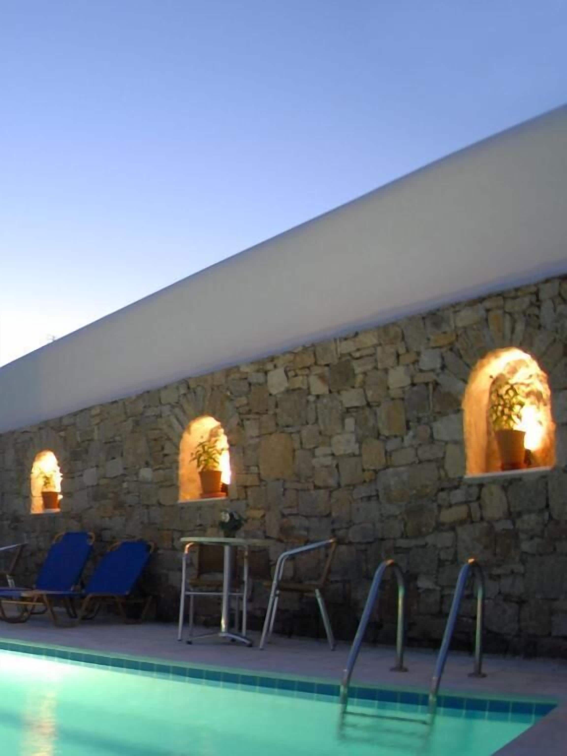 A poolside area with stone walls, blue lounge chairs, and a pool.