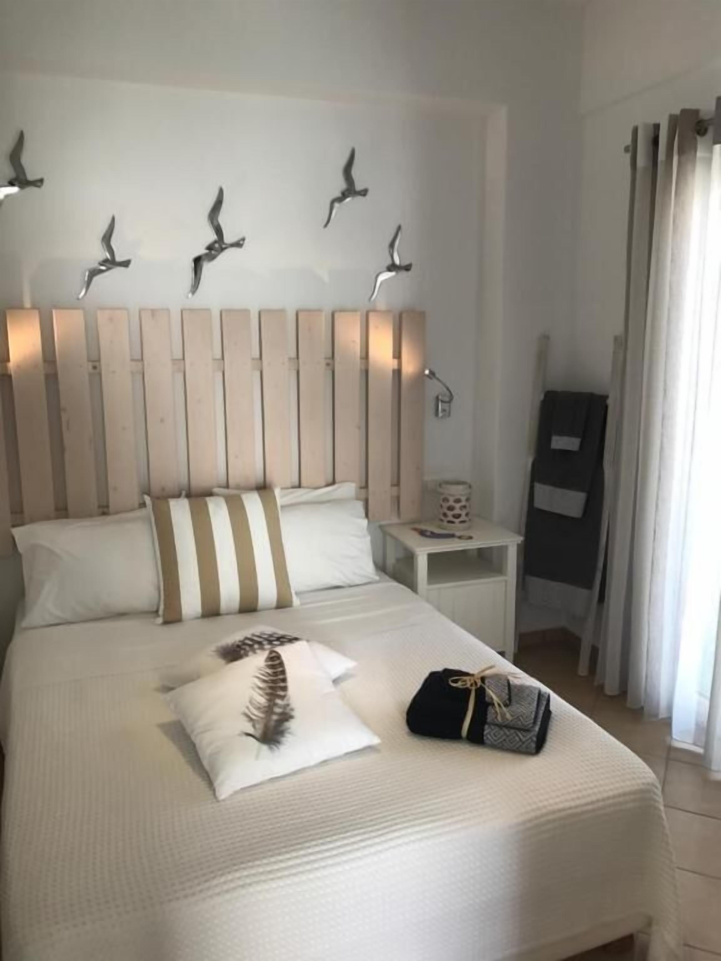 A neatly made bed with a pillow and a feather. There is a nightstand with a lamp and a small table with a decorative item.