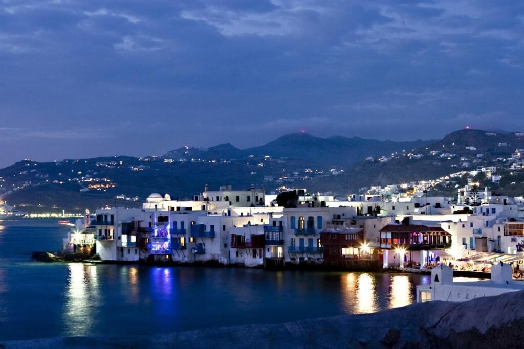 A coastal town with white buildings, a harbor, and a mountain in the background.