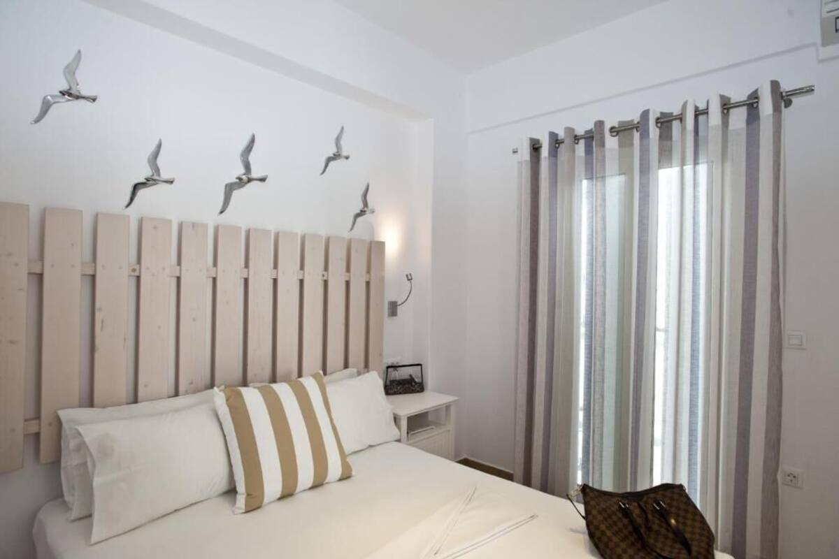 A bedroom with a wooden headboard, a bed with white and striped pillows, a nightstand with a radio, and a window with striped curtains.