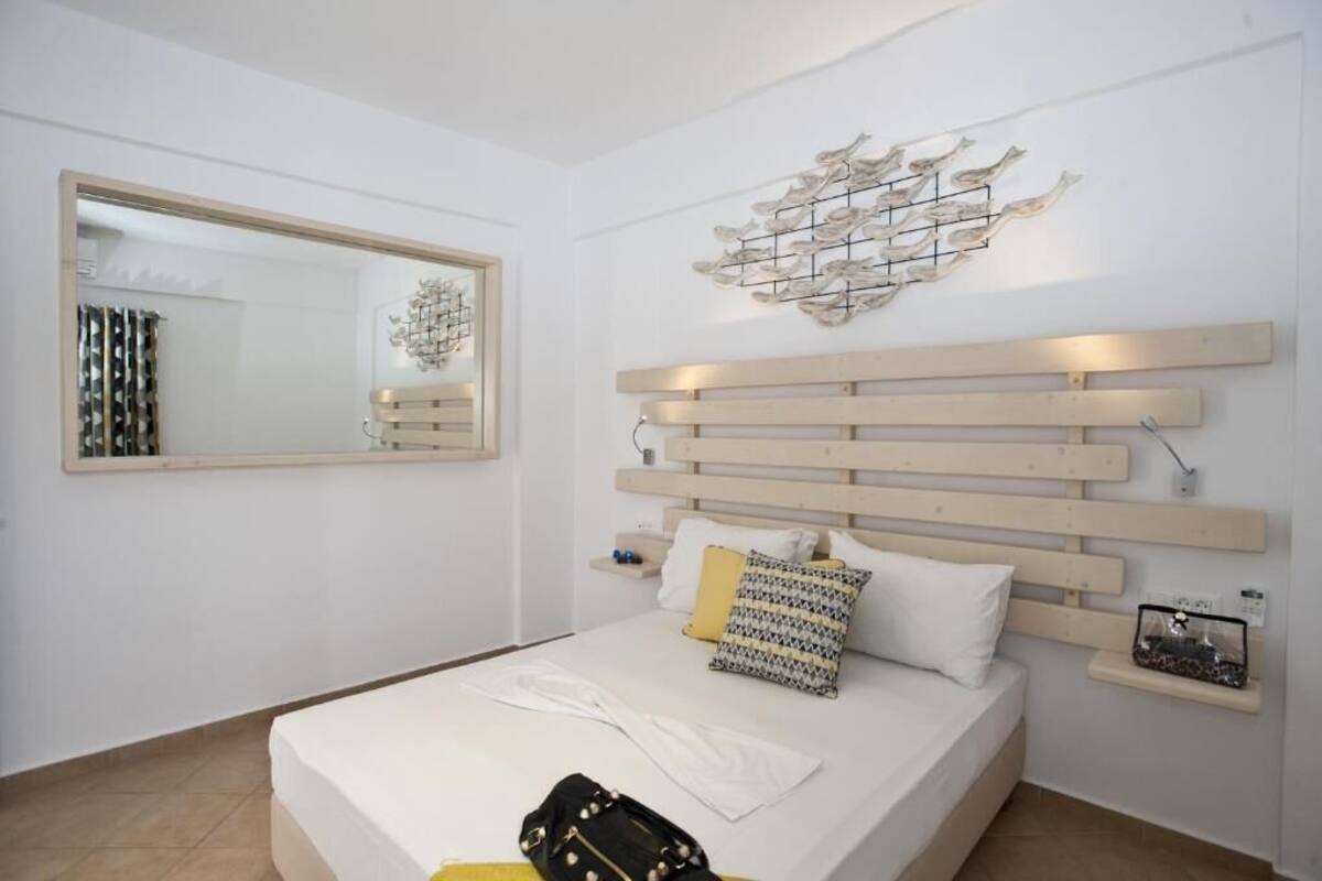 A modern bedroom with a large bed, a wooden headboard, a wall-mounted mirror, and a decorative wall piece.