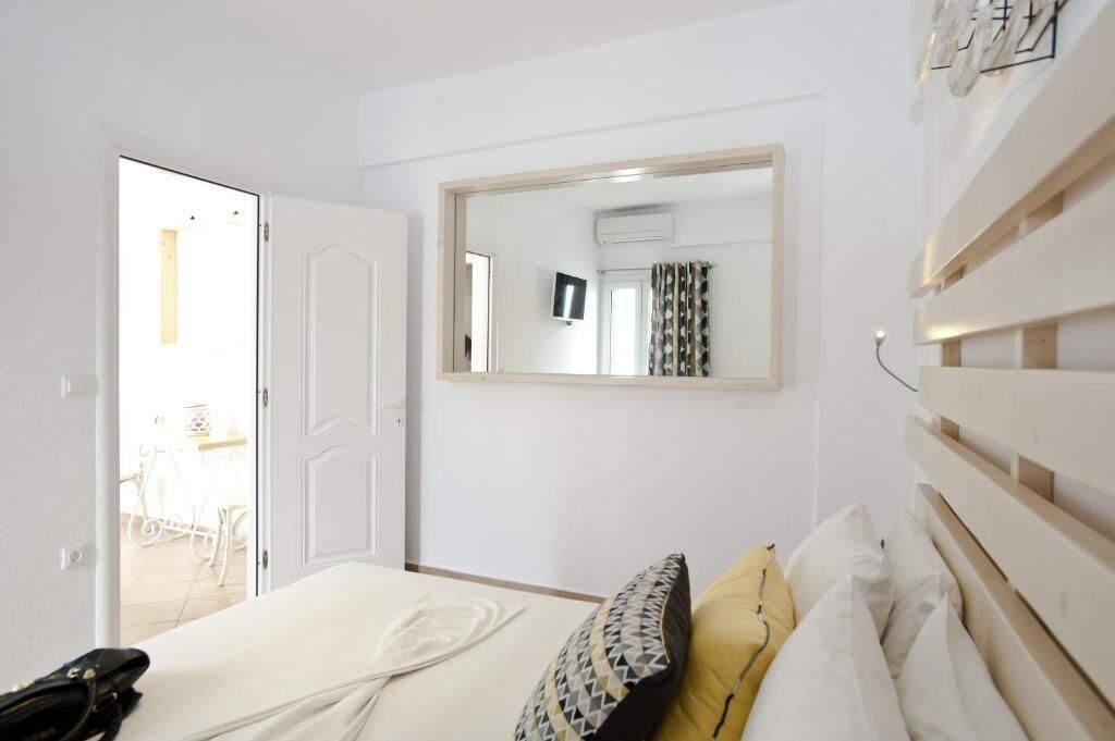 A hotel room with a bed, a mirror, a television, and a door leading to a balcony.