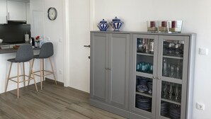 A modern kitchen with a built-in stove, two bar stools, a cabinet with glass doors displaying dishes and glasses, and a wall-mounted air conditioner. - Waterfront apartment Levante beach , in waterfront promenade. Great views (Benidorm)
