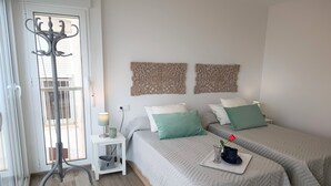 A bedroom with two beds, a bedside table with a lamp, a coat rack, and decorative wall art. - Waterfront apartment Levante beach , in waterfront promenade. Great views (Benidorm)