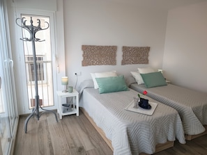 A bedroom with two beds, a bedside table with a lamp, a coat rack, and decorative wall art.