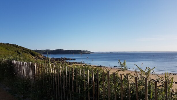 A coastal view with a wooden fence, beach, and distant hills. - Cosy house with fireplace (Lannion)