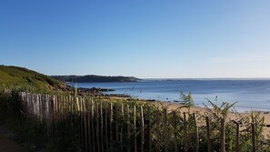 Vista costeira com cerca de madeira, praia e colinas ao longe.