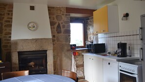 A kitchen with a stone wall, a fireplace, a dining table with chairs, a microwave, a coffee maker, and a dishwasher. - Cosy house with fireplace (Lannion)