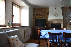 Uma sala de estar acolhedora com parede de pedra, lareira, televisão e um espaço de jantar com toalha xadrez azul.