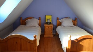 A room with two wooden beds, a nightstand with a lamp, and a framed picture on the wall. - Cosy house with fireplace (Lannion)