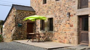 A stone building with a wooden deck, a table with chairs, and a green umbrella. - Cosy house with fireplace (Lannion)