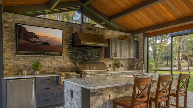 Una cocina moderna con una isla de piedra, electrodomésticos de acero inoxidable y un televisor grande montado en la pared.