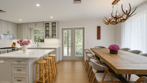 Una cocina moderna con una isla grande, taburetes de bar y una zona de comedor con mesa y sillas de madera.