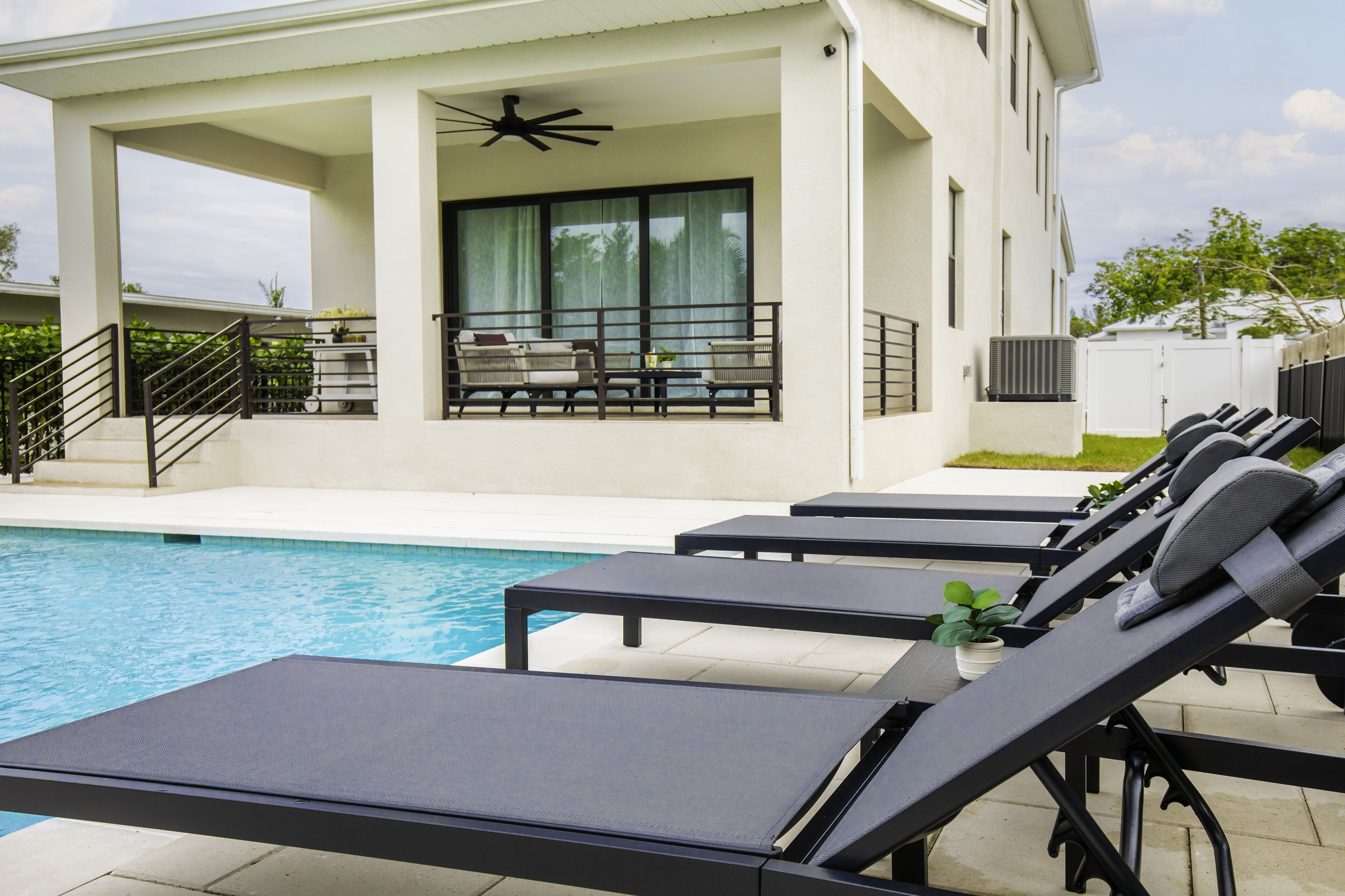 A poolside area with lounge chairs, a covered seating area with a ceiling fan, and a view of the pool.
