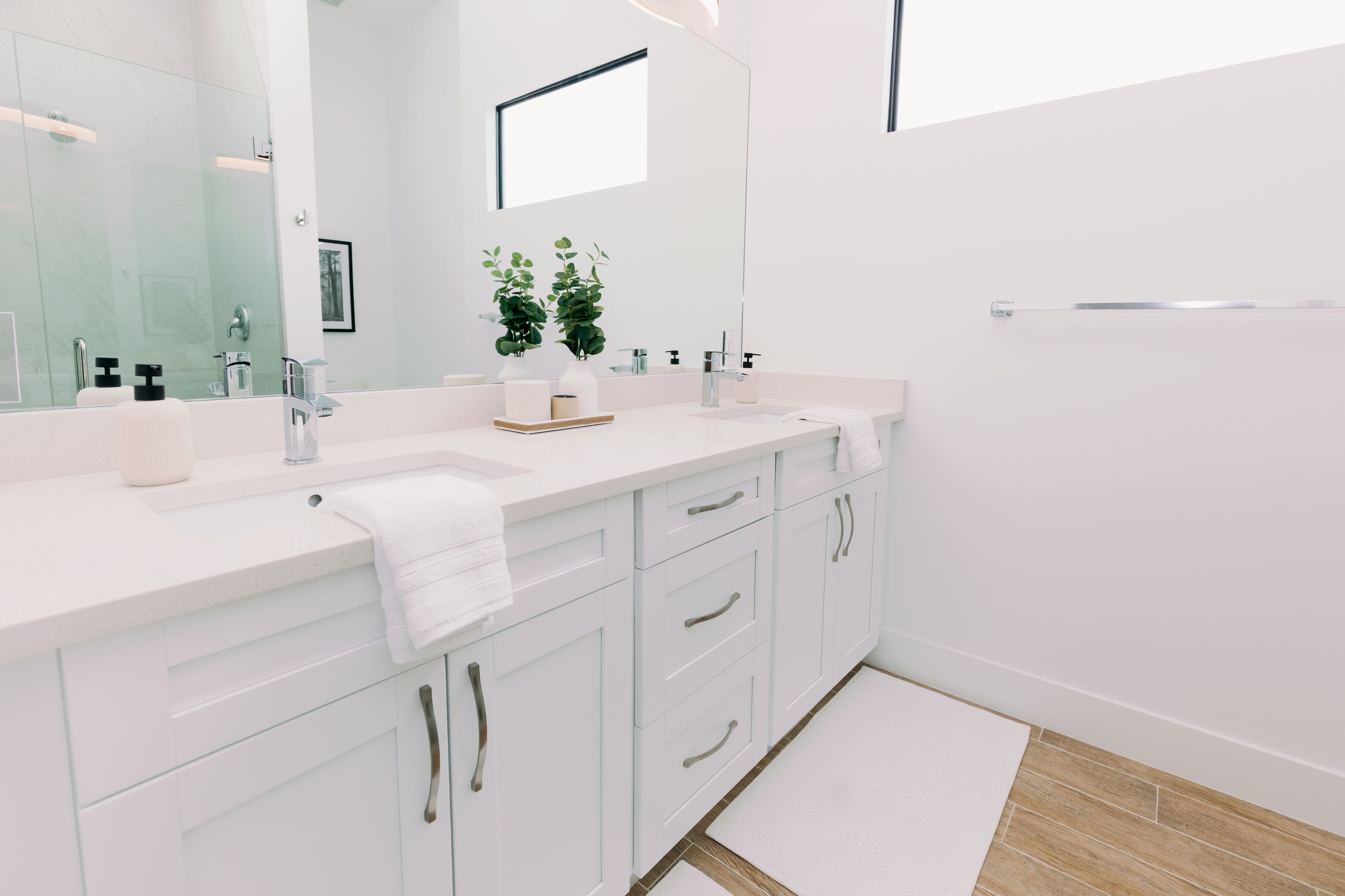 A modern bathroom with white cabinetry, a large mirror, and a small potted plant.