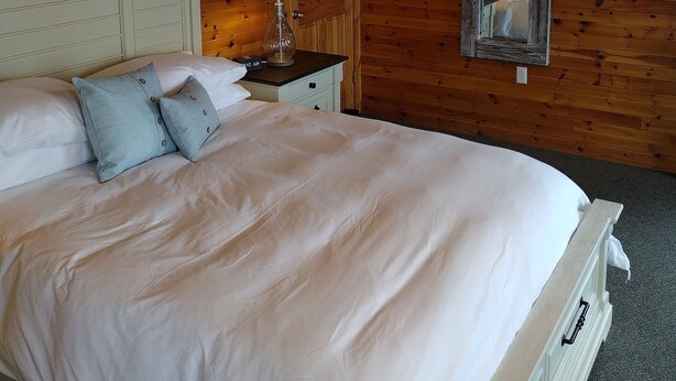 Een slaapkamer met houten lambrisering, een bed, kussens, een nachtkastje, een lamp en een spiegel.