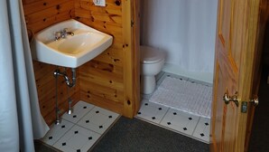 Een houten badkamer met een wastafel, twee haardrogen, een toilet en een douchegordijn.