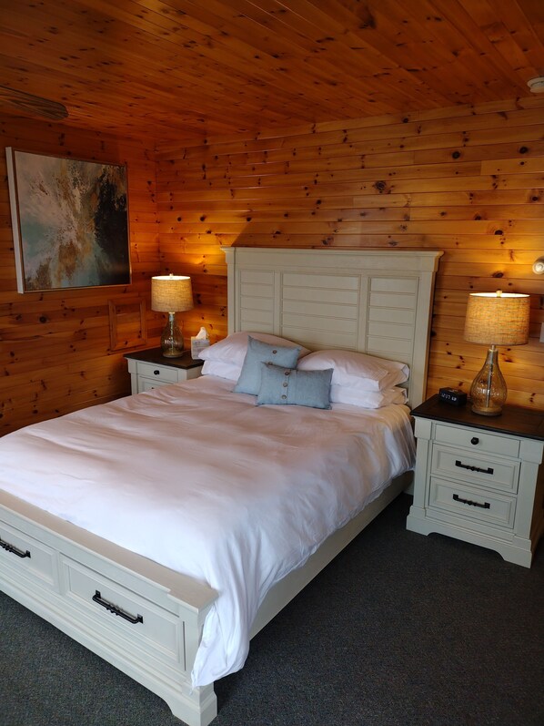 A wooden-paneled bedroom with a bed, two bedside tables, and a wall-mounted lamp.