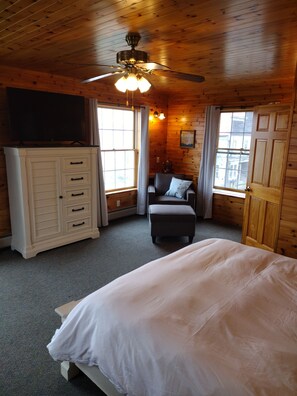 A bedroom with a bed, a television on a cabinet, a ceiling fan, and windows with curtains.