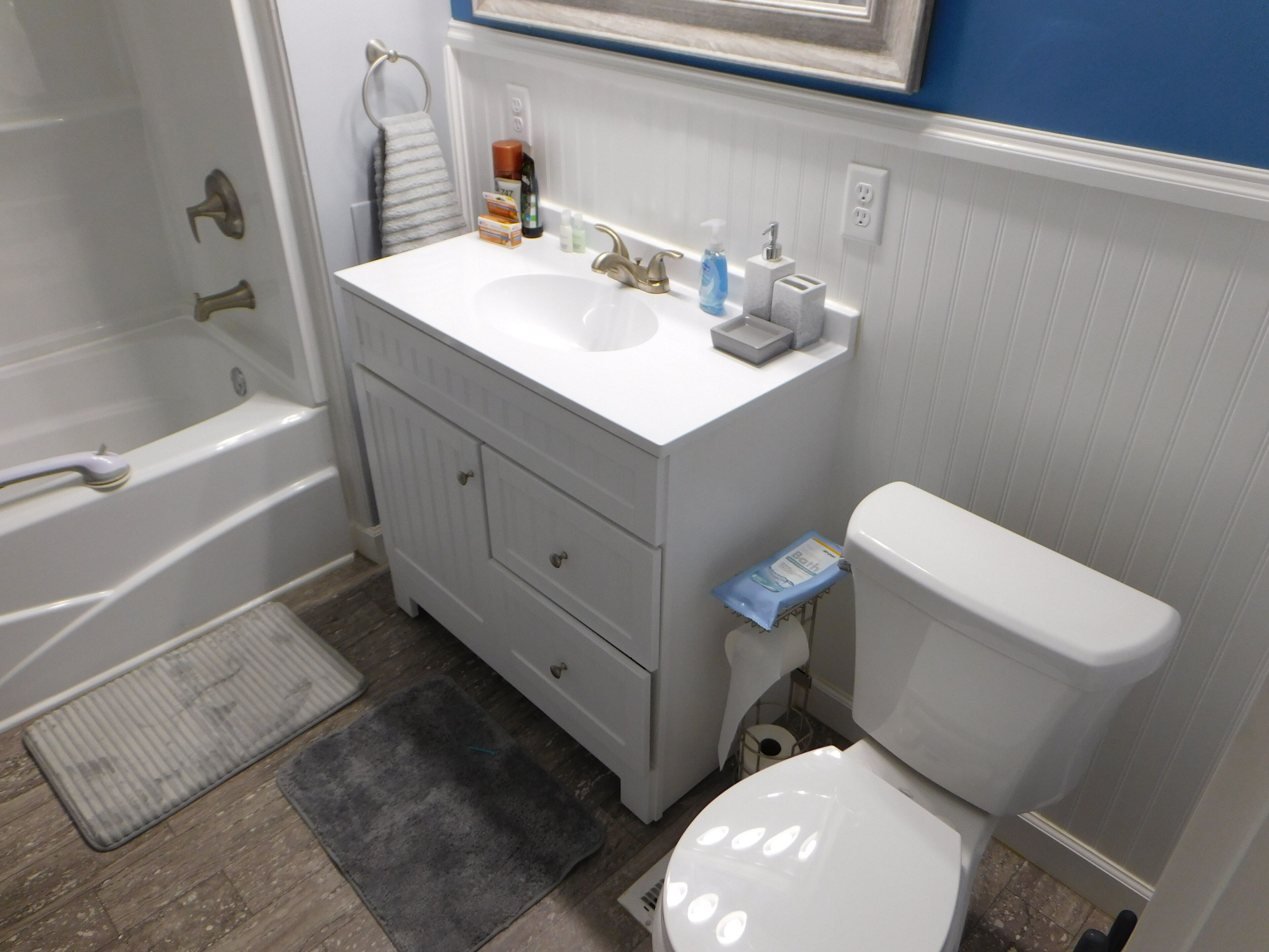 A bathroom with a bathtub, a sink with a mirror above it, a toilet, and a small trash bin.