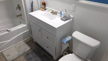 A bathroom with a bathtub, a sink with a mirror above it, a toilet, and a small trash bin.