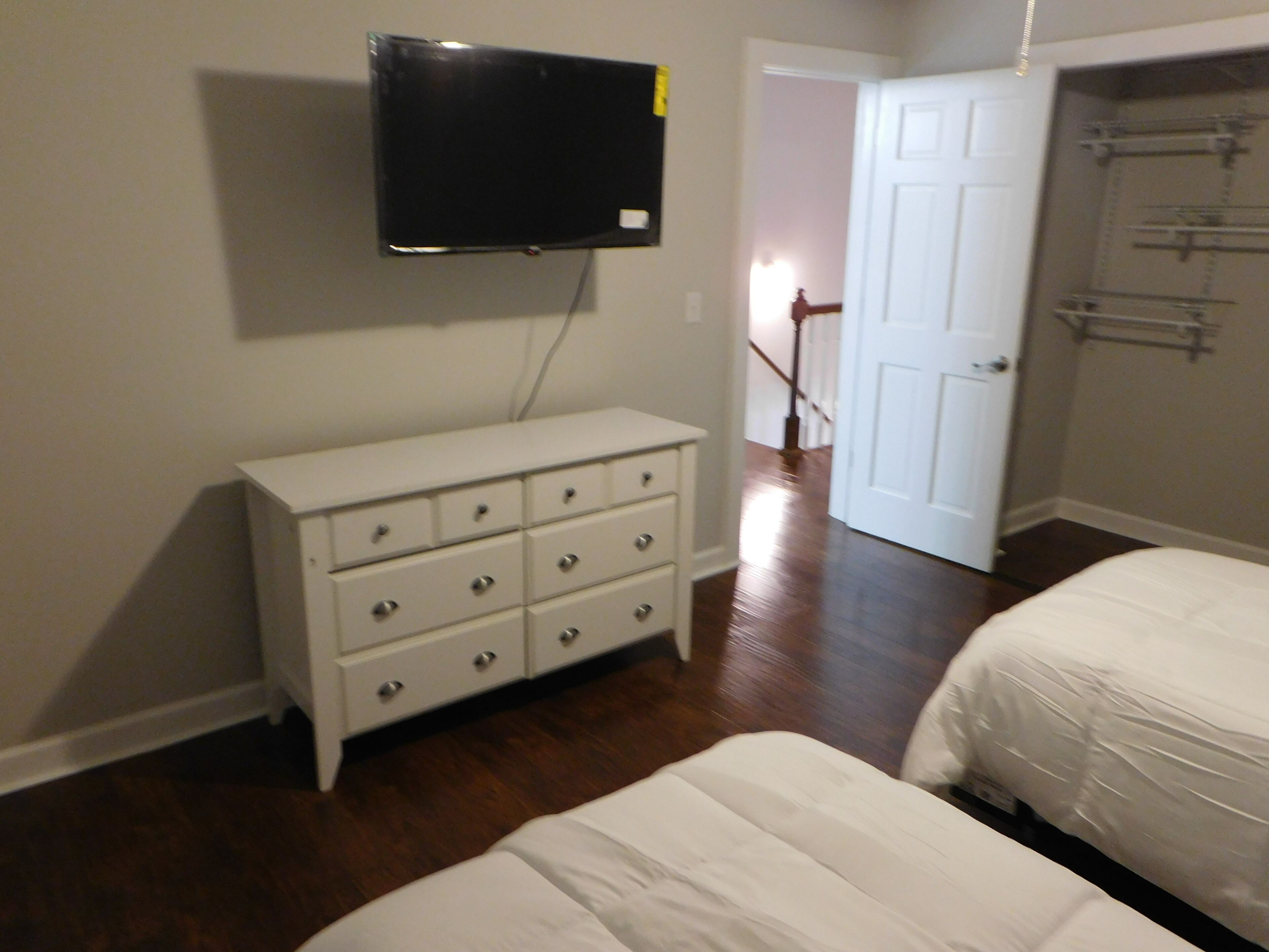 A bedroom with a white dresser, a bed, and a television mounted on the wall.