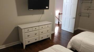 A bedroom with a white dresser, a bed, and a television mounted on the wall.