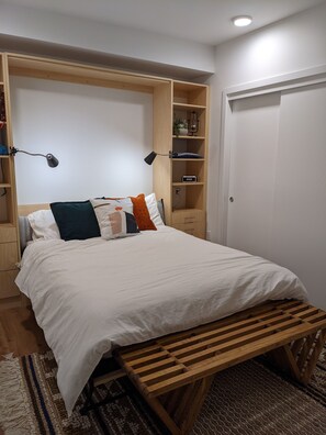 A bedroom with a large bed, a wooden bench, and built-in shelves with a lamp. - Space Needle and Mountain View. Top-Floor Condo (Seattle)