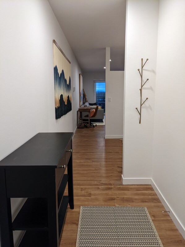A modern interior with a wooden floor, a black desk, a patterned rug, and a wall-mounted art piece. - Space Needle and Mountain View. Top-Floor Condo (Seattle)
