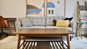 A modern living room with a grey sofa, a wooden coffee table, and a painting of a blue and white building. - Space Needle and Mountain View. Top-Floor Condo (Seattle)