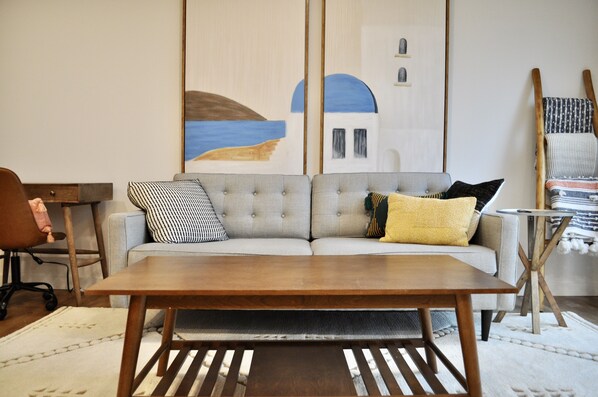 A modern living room with a grey sofa, a wooden coffee table, and a painting of a blue and white building. - Space Needle and Mountain View. Top-Floor Condo (Seattle)