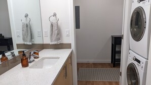 A modern bathroom with a white countertop, a sink, a mirror, and a washing machine. - Space Needle and Mountain View. Top-Floor Condo (Seattle)