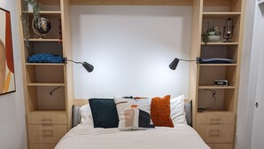 A bedroom with a bed, wooden headboard, built-in shelving, and a bedside table. - Space Needle and Mountain View. Top-Floor Condo (Seattle)