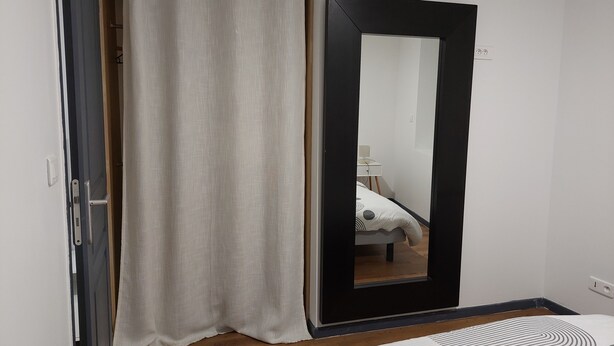 Une chambre à coucher avec un lit, une table de chevet, un miroir et un rideau.