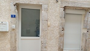 Une façade d’immeuble avec une porte numérotée, une petite fenêtre avec des volets et un coffret de raccordement.