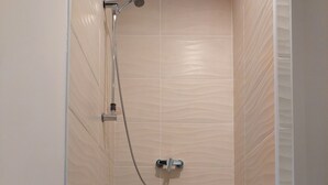 Une douche équipée d’un pommeau de douche à main et d’un robinet fixé au mur.