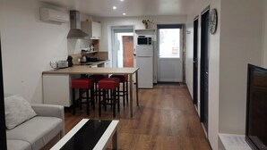 Un espace de vie compact comprenant un coin cuisine, un coin repas avec des tabourets de bar rouges, un canapé et un téléviseur.