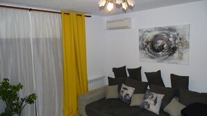 A living room with a sofa, yellow curtains, a potted plant, and a wall-mounted air conditioner.