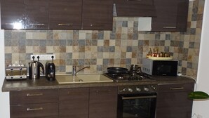 A kitchen with dark wood cabinets, a tiled backsplash, a gas stove, a microwave, a toaster, and a kettle.
