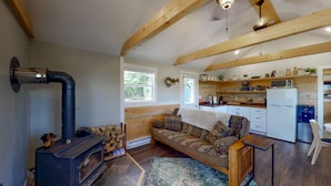 Uma sala de estar acolhedora com sofá, lareira e área de cozinha com vigas de madeira e geladeira.