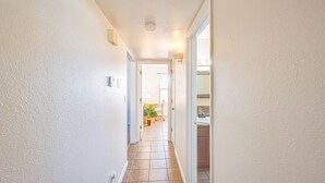 A hallway with white walls and tiled flooring leading to a bathroom with a sink and mirror. - Sunny, functional, Central NW --Super Clean (Albuquerque)