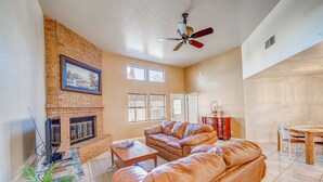 A living room with a brick fireplace, leather sofa, and a dining area with a wooden table and chairs. - Sunny, functional, Central NW --Super Clean (Albuquerque)