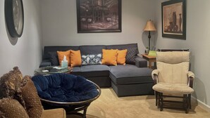 Ein modernes Wohnzimmer mit einer Eckcouch, einem blauen Sessel, einem beigen Ohrensessel und einem runden Couchtisch.