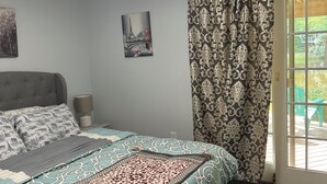 Ein Schlafzimmer mit einem Bett, einer Bank, einer Lampe, einem Gemälde und einem Fenster mit Vorhängen.