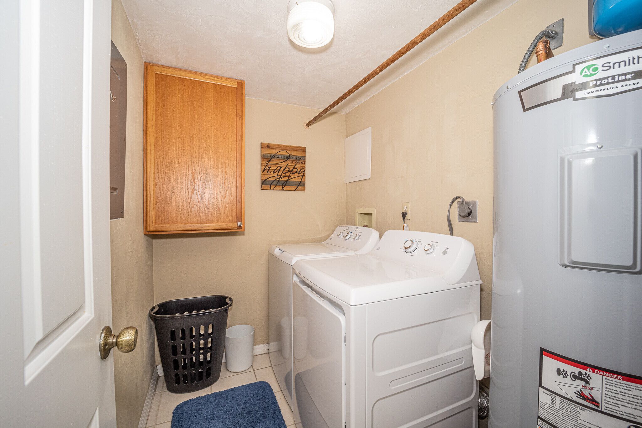 A laundry room with a washing machine, a dryer, a wooden cabinet, and a blue rug.